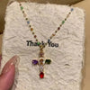 A colorful zircon cross pendant necklace with multicolored beads on a gold chain displayed on a white fluffy surface.
