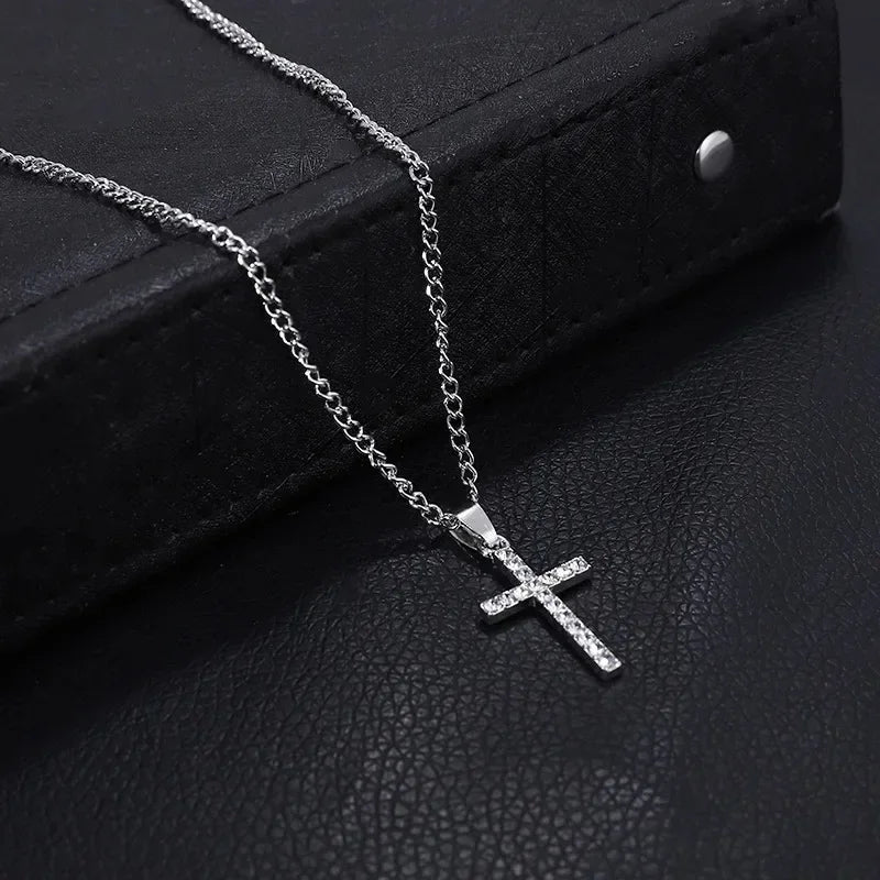 A silver stainless steel cross pendant necklace with a chain is displayed on a black surface.