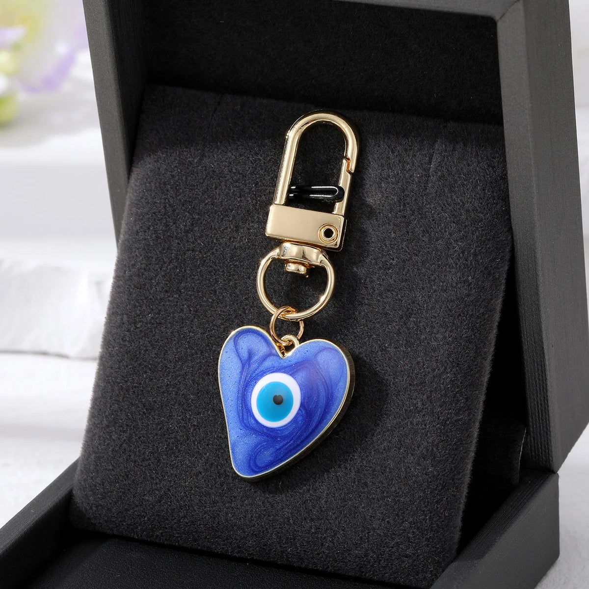 Gold heart-shaped keychain with a blue and white evil eye design displayed in a black velvet box.
