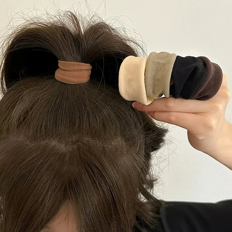 A hand is holding several extra-wide elastic hair bands in various neutral and earth tones against a person's dark brown hair