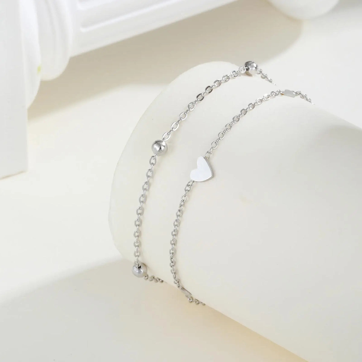 Silver stainless steel heart double chain anklet set displayed on a white surface.