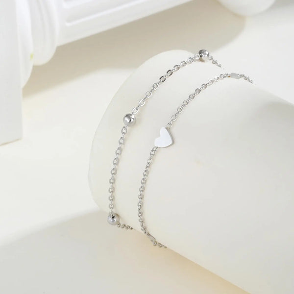 Silver stainless steel heart double chain anklet set displayed on a white surface.