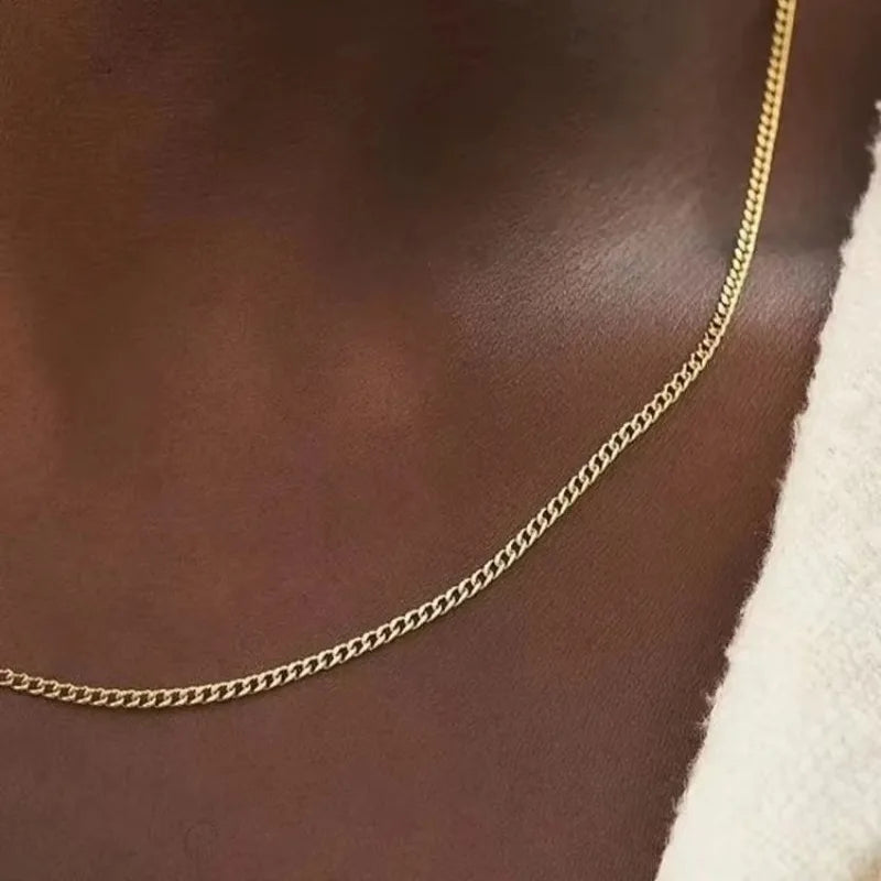 Un collier de chaîne cubaine en acier inoxydable de couleur or posé sur un tissu brun foncé.