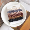 A pack of six satin hair scrunchies in various muted and earthy tones displayed on a white plate.