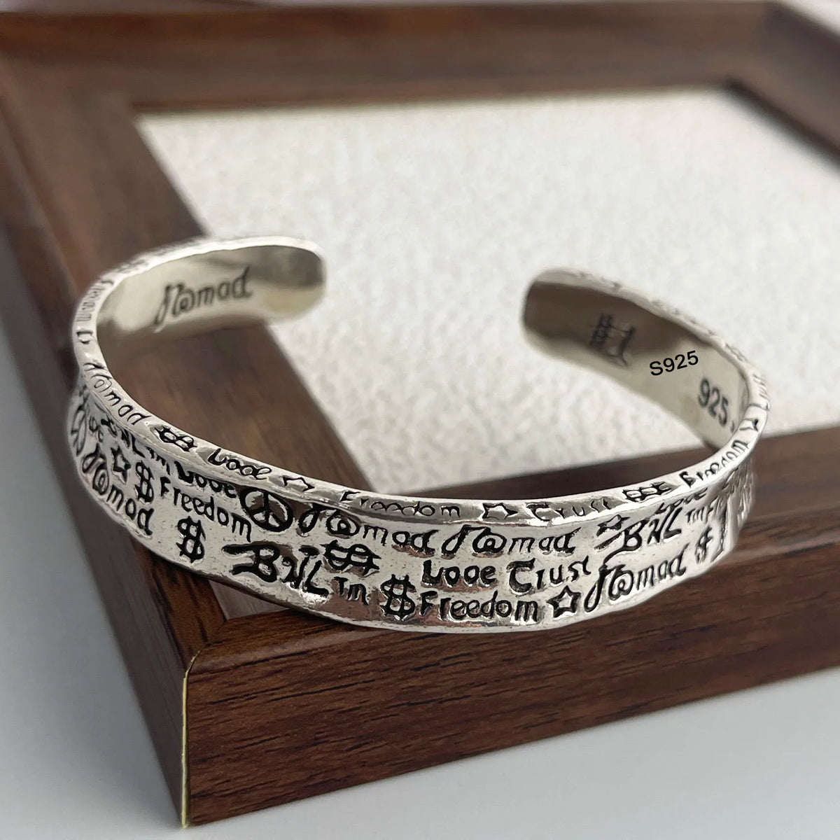 A sterling silver charm bracelet is displayed in a wooden frame, featuring various charms and a stamped maker's mark.