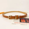 A brown slim PU leather belt with a vintage gold-toned buckle lying on a piece of paper.