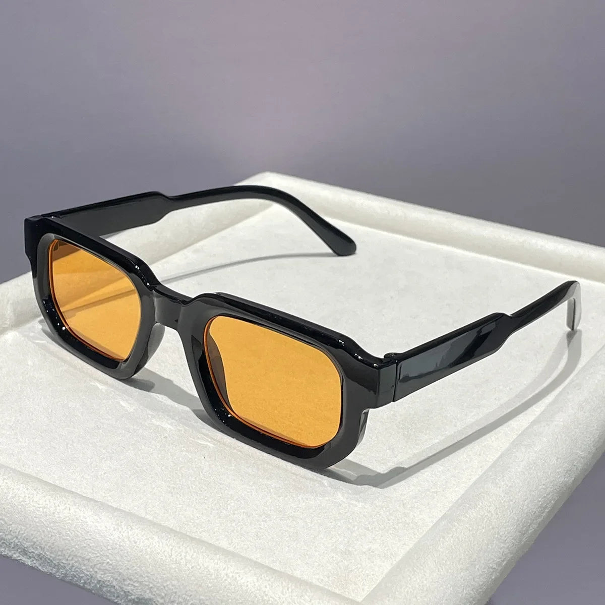 Black retro square sunglasses with orange tinted lenses resting on a white surface