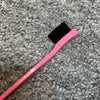 Pinkes und schwarzes professionelles doppseitiges Augenbrauenkamm auf grauer, strukturierter Oberfläche.