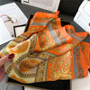 An orange and gold patterned silk scarf draped on a dark tray.