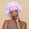A woman wearing a purple satin sleep bonnet with a matching wrap band.