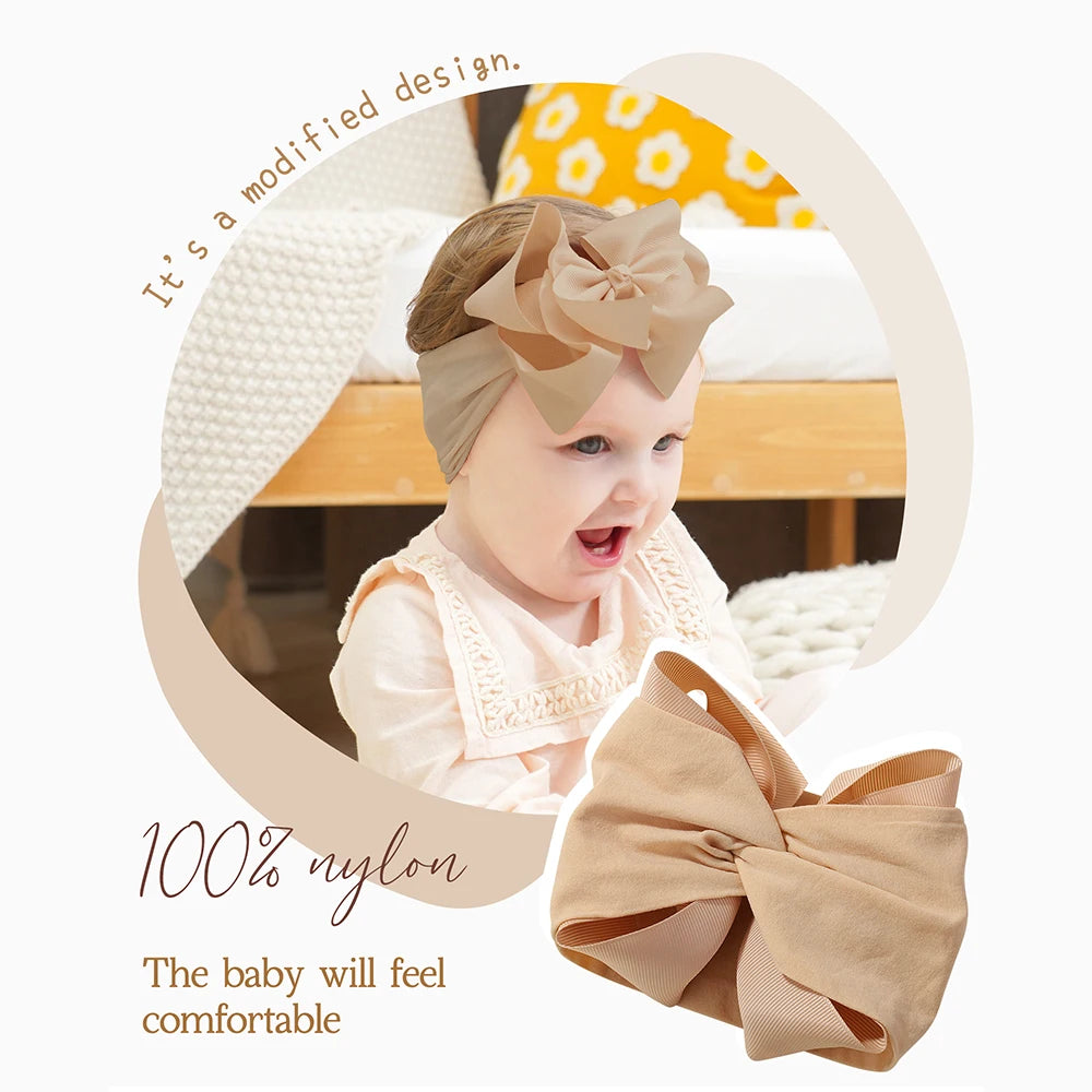A baby wearing a beige soft headband with a chunky hair bow, shown in a light-colored room.