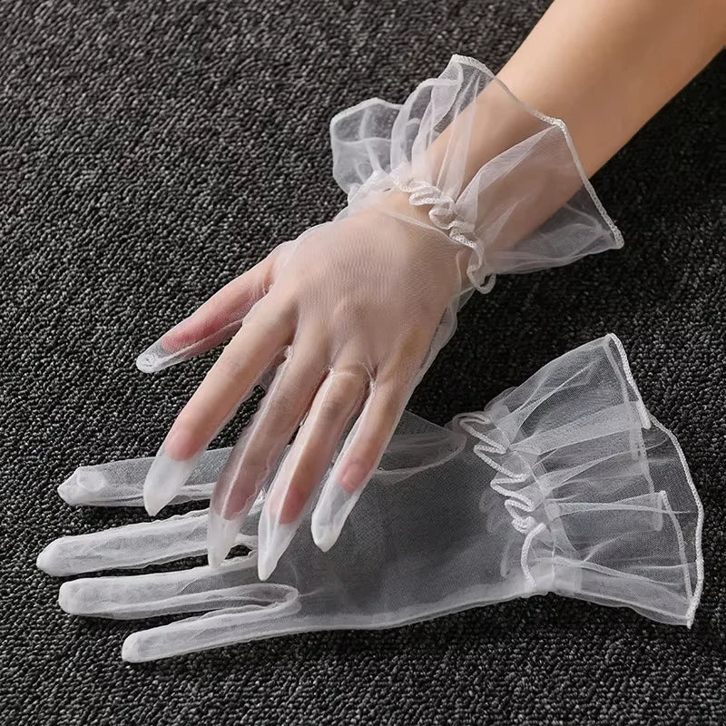 Clear lace tulle finger gloves worn on a hand against a dark background.