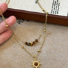 A gold-toned necklace featuring a tiger eye sunflower pendant, displayed on a beige fabric.