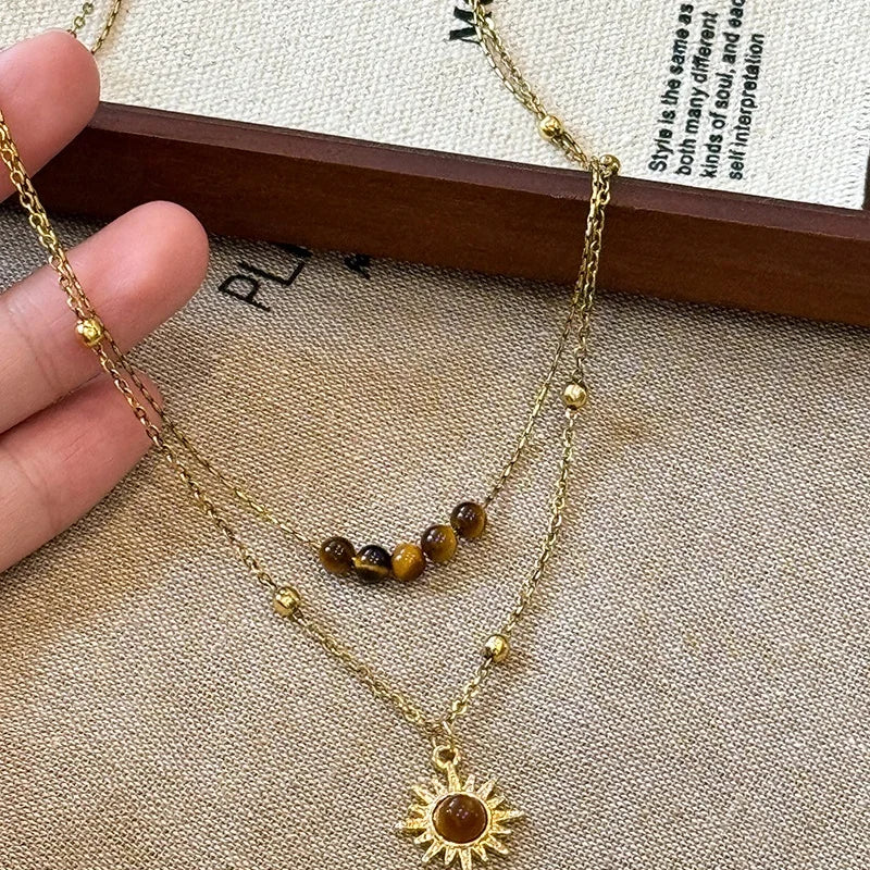 A gold-toned necklace featuring a tiger eye sunflower pendant, displayed on a beige fabric.