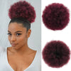 A woman shows off a reddish-purple kinky drawstring ponytail extension, featuring a voluminous, textured hair piece.