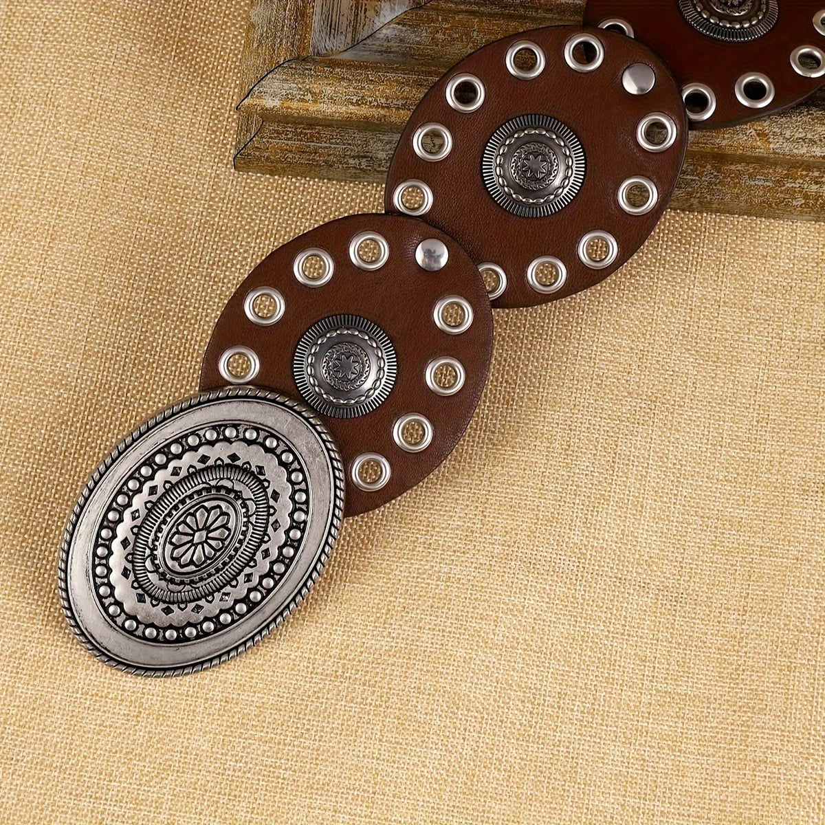 A set of five brown and silver floral oval waist belts arranged diagonally on a beige fabric background.