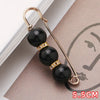 Gold-toned safety pin with three black beads and gold accents displayed on a brown card.
