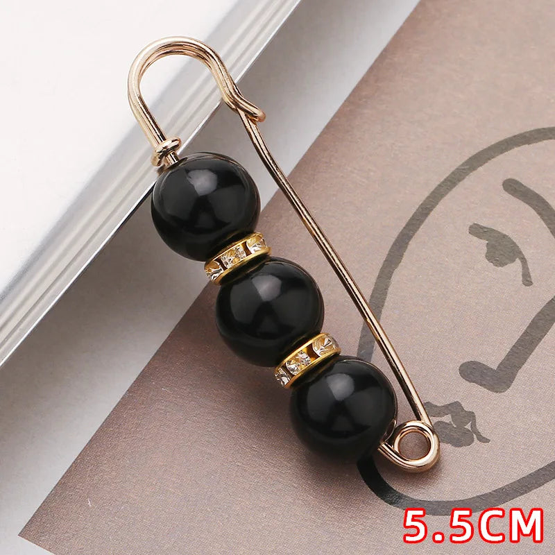 Gold-toned safety pin with three black beads and gold accents displayed on a brown card.