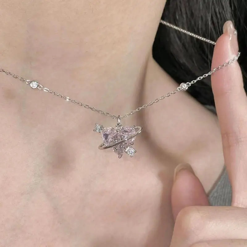 A delicate silver necklace featuring a pink heart zircon charm and a chain, worn against a person's neck.