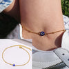 Gold snake chain anklet with a blue bead worn on a woman's ankle.