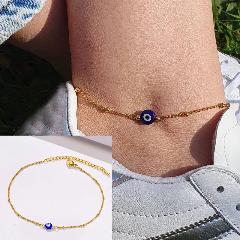 Gold snake chain anklet with a blue bead worn on a woman's ankle.
