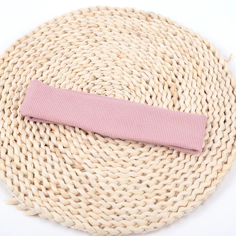 A pink knitted elastic headband lying on a natural woven mat.