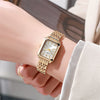 A close-up of a gold plated quartz fashion watch worn on a wrist against a light background.