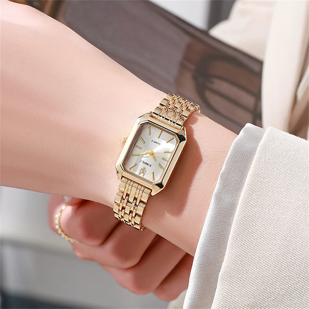 A close-up of a gold plated quartz fashion watch worn on a wrist against a light background.