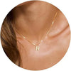 A close-up of a gold plated alphabet initial necklace resting on a person's neck and collarbone.
