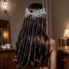 El largo cabello oscuro de una mujer está adornado con una diadema nupcial hecha de borlas de plata y cadenas de aguja.