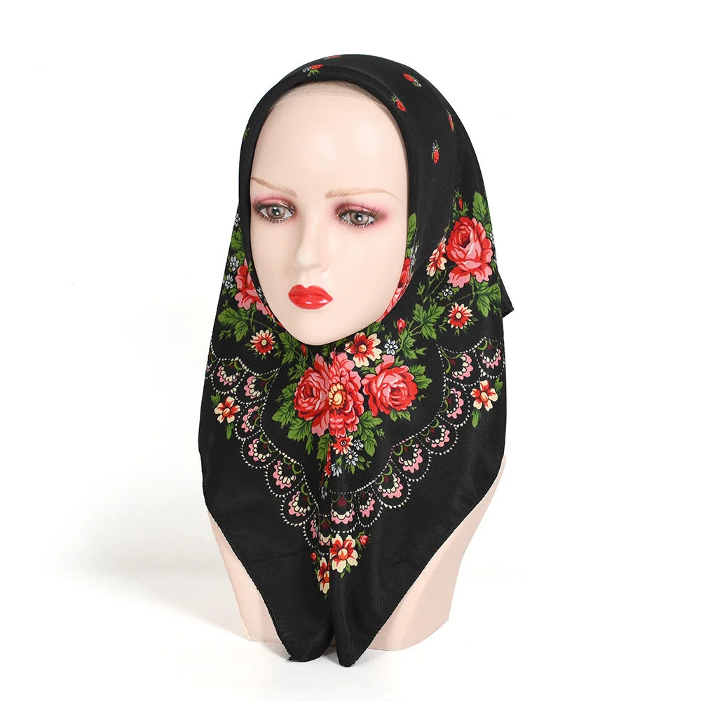 A black square scarf with a luxury floral print featuring red roses and green foliage displayed on a mannequin's head.