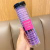 Una mano sostiene un recipiente de plástico transparente lleno de gomas para el cabello onduladas y rayadas de color morado, 