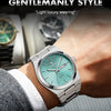 A close-up of a silver-toned men's quartz wristwatch with a light blue dial and green accents on a wrist.