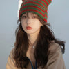 A woman wearing a green and red crocheted cat ears beanie hat and a beige sweater.