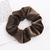 A close-up shot of a dark brown velvet scrunchie, showing its texture and gathered fabric.