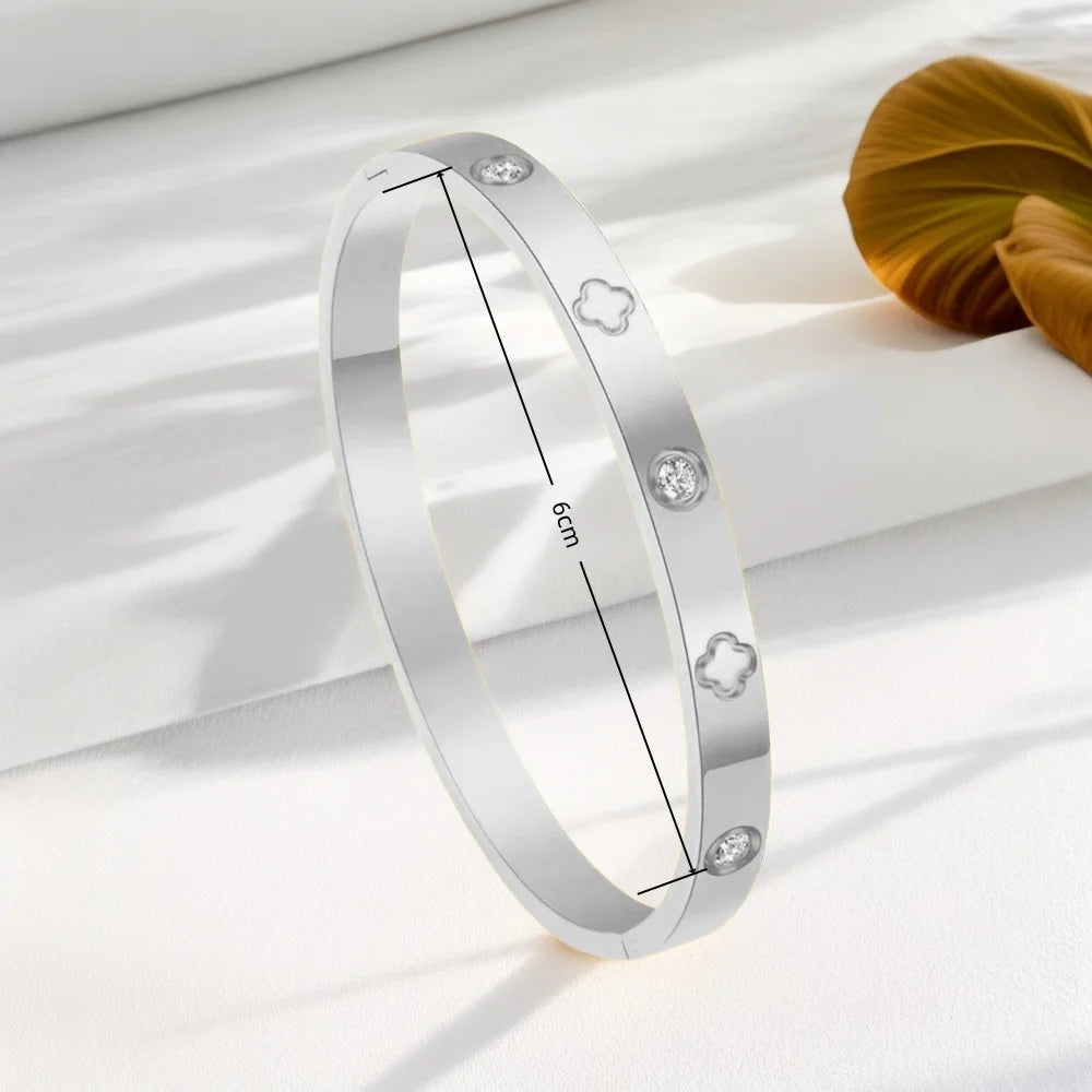 Silver stainless steel bangle bracelet featuring four-leaf clover and nail charms