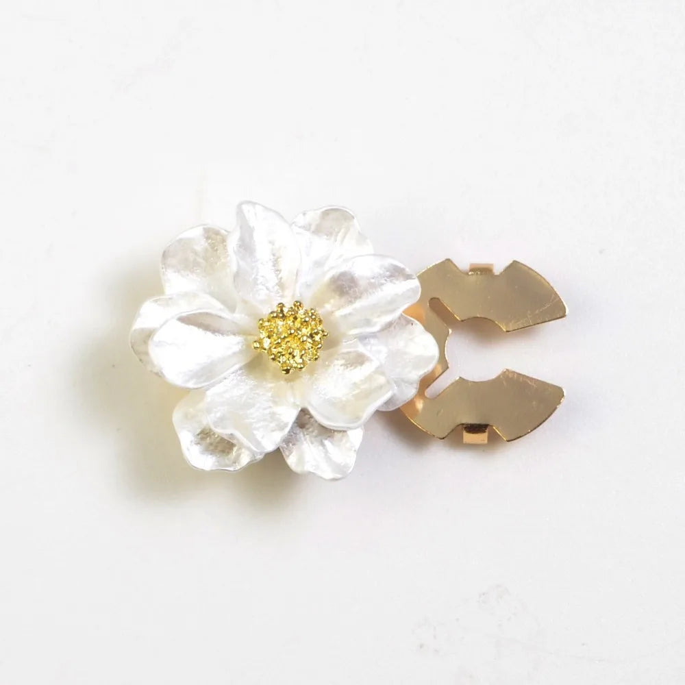 A white, pearlescent flower button cover with a gold center and a gold C-shaped clasp.