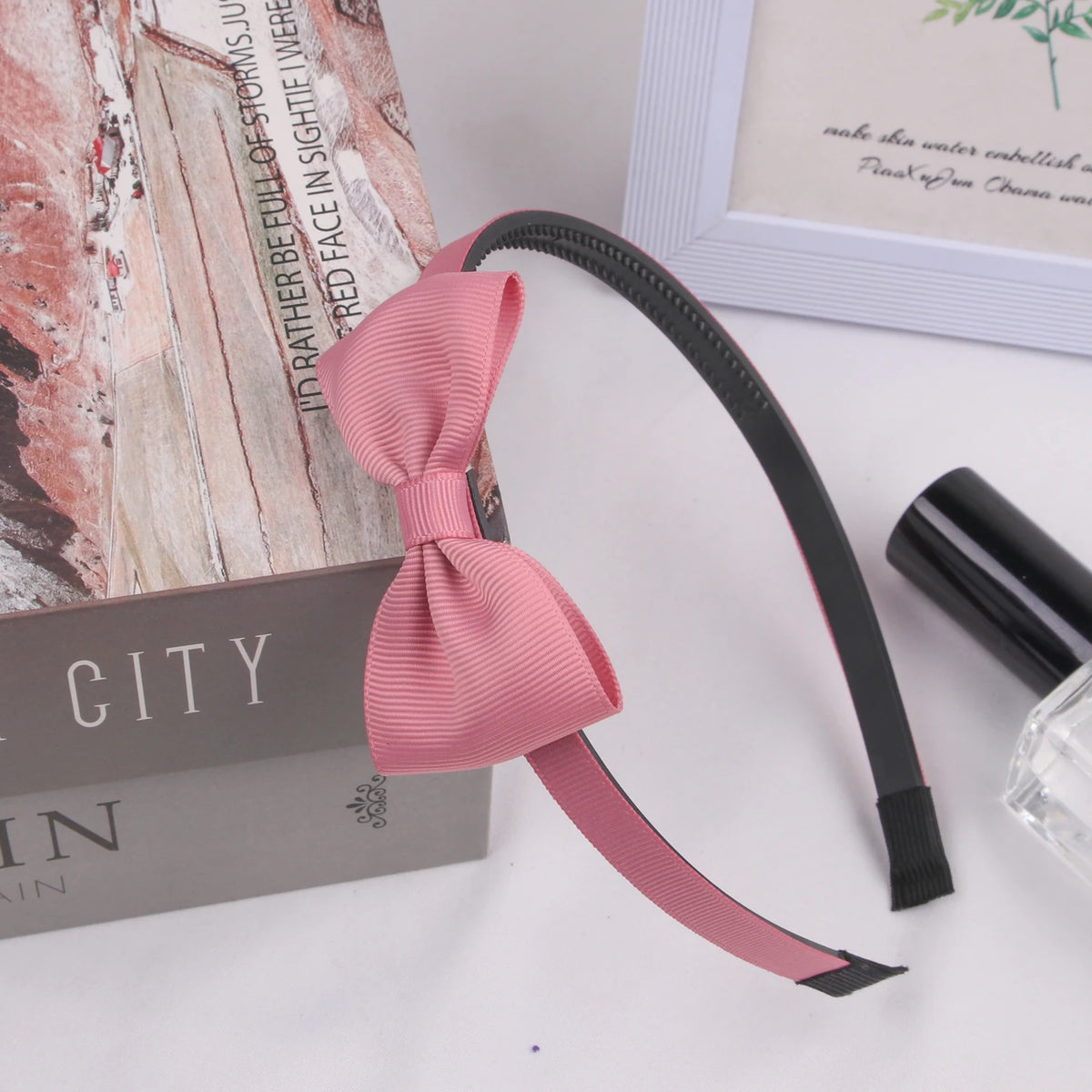 A pink grosgrain ribbon hair bow is displayed next to a box and a glass.