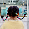 A person's dark hair is styled with colorful nylon elastic hair cords in a braided design.