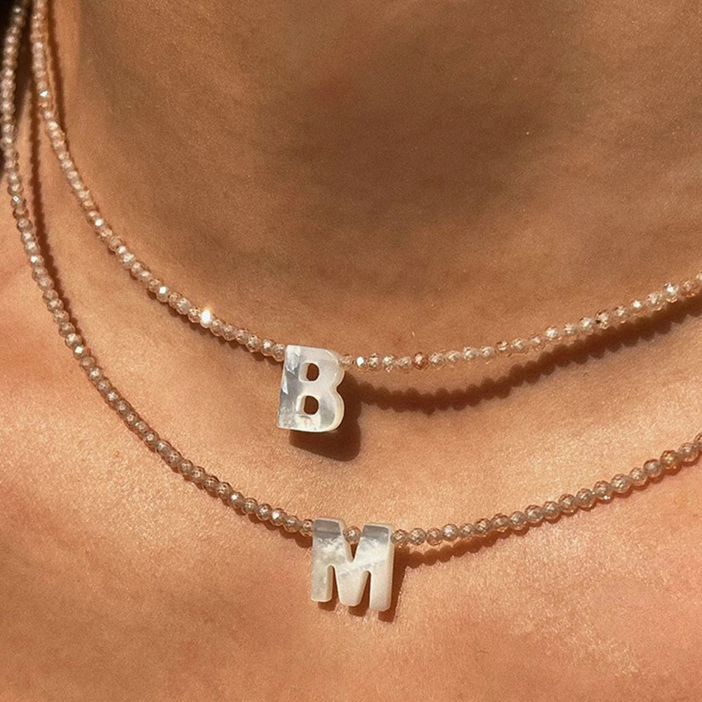 A close-up of a delicate crystal necklace featuring a letter B and an M on fine chains.