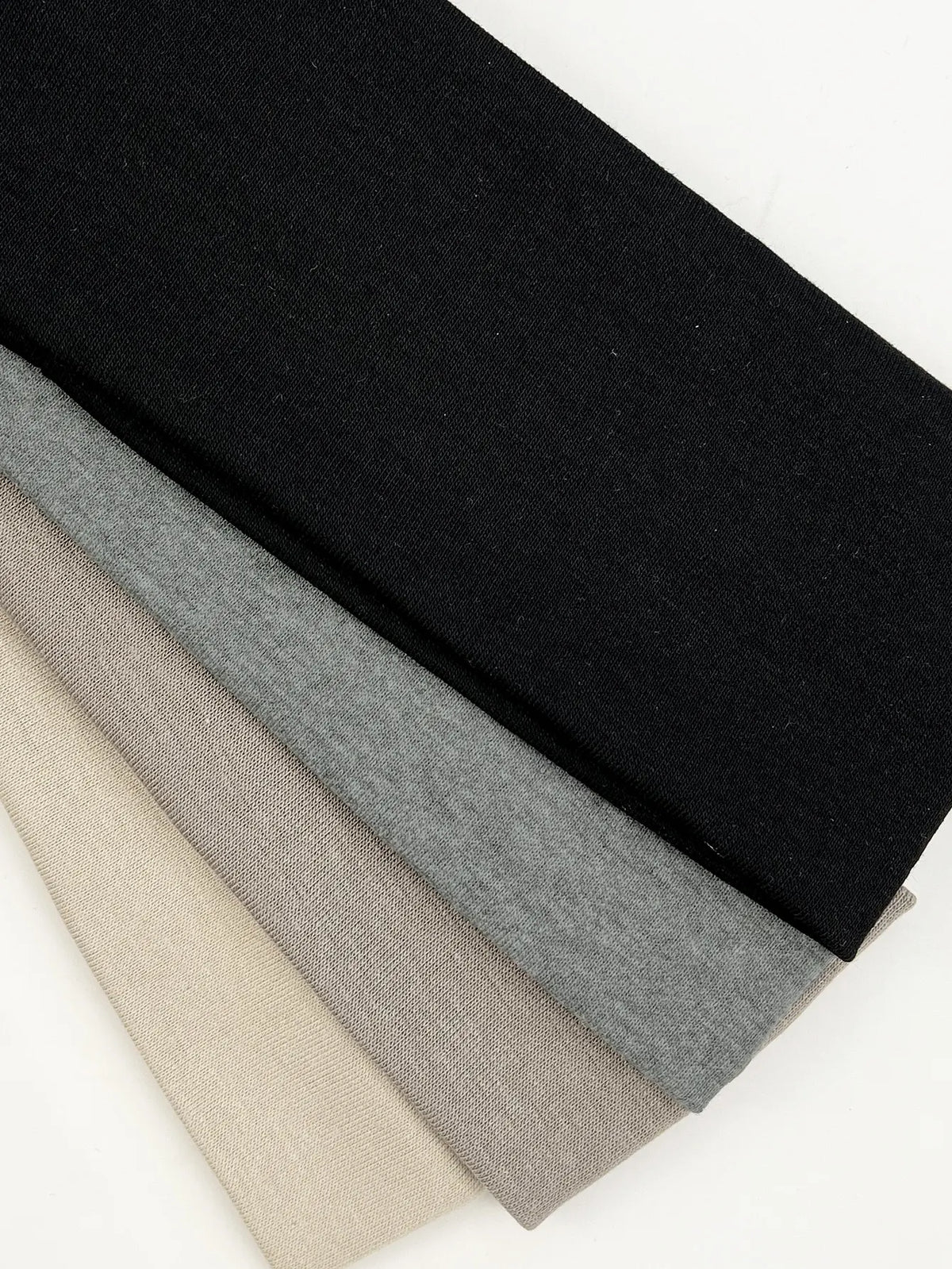 A set of four knitted hair bands in black, gray, beige, and light tan laid diagonally.