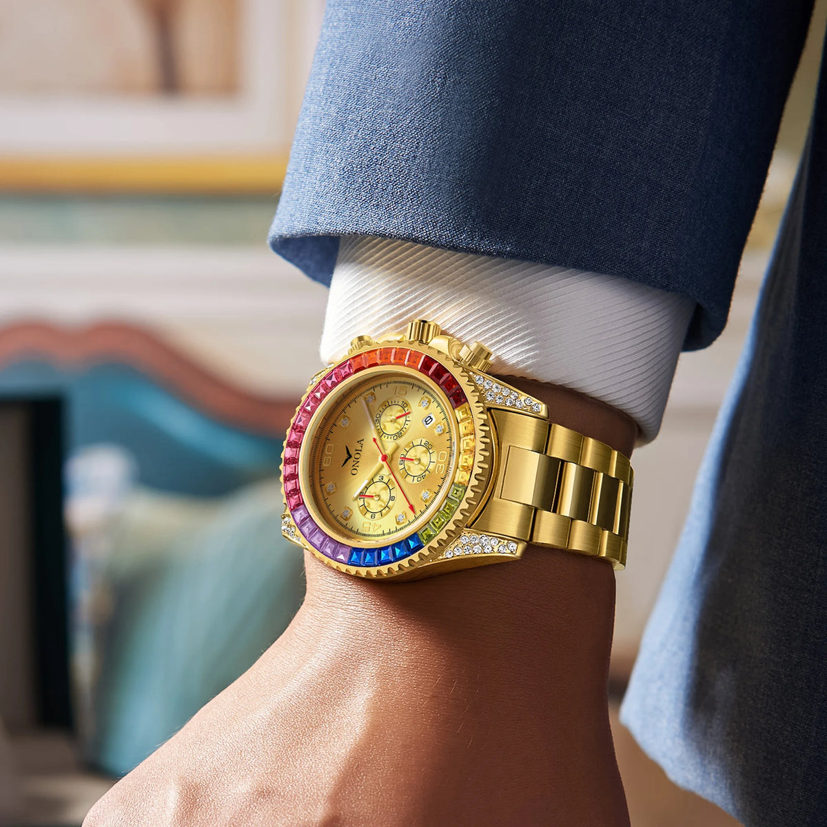 A close-up of a men's gold quartz watch with diamond accents worn on a wrist, visible under a blue suit sleeve.