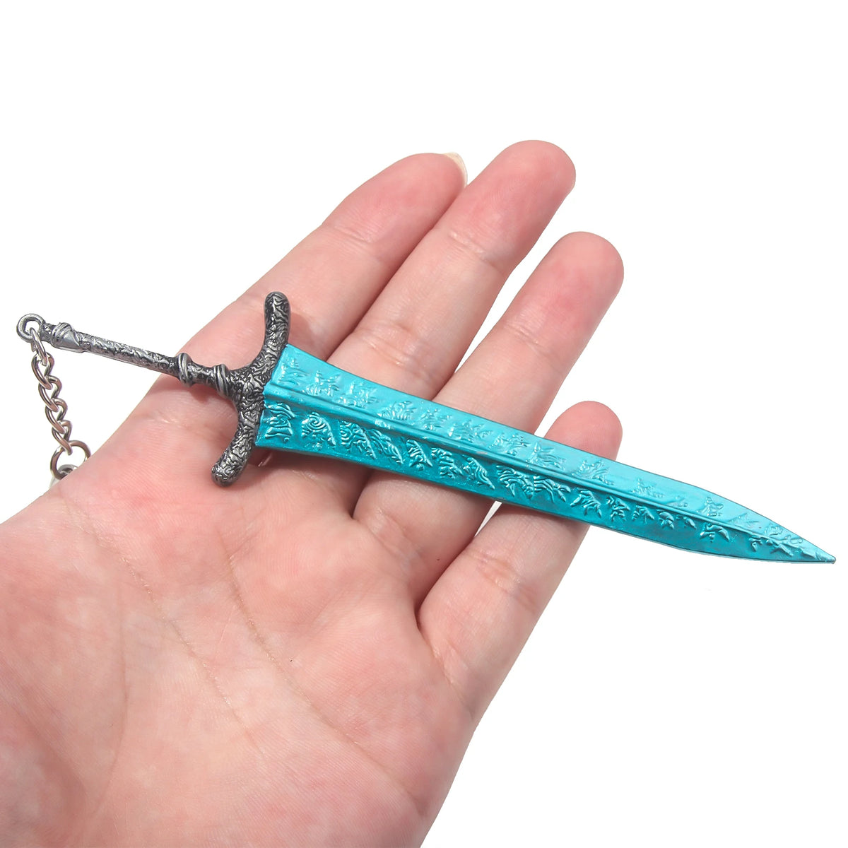 A hand holds a silver dagger-shaped pendant with a turquoise blade and a chain.