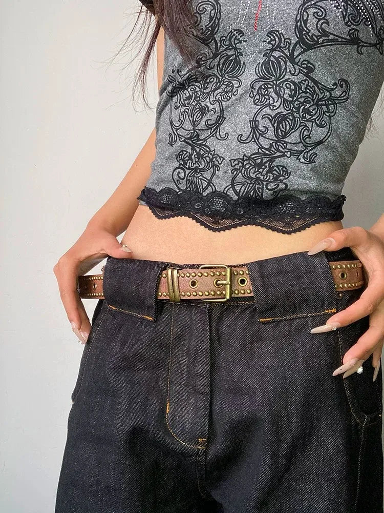 A close-up of a woman wearing a black top and dark jeans with a brown belt featuring bronze rivets.