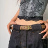 A close-up of a woman wearing a black top and dark jeans with a brown belt featuring bronze rivets.