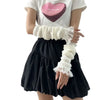 A person is wearing white fingerless arm warmers and a black skirt, with a white t-shirt featuring a pink heart design.