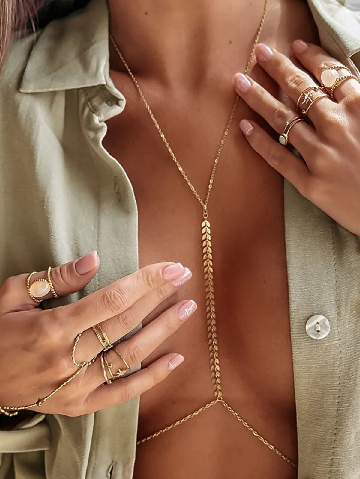 A close-up of a woman wearing a gold minimalist wheat body chain necklace on her chest, paired with a light green shirt.