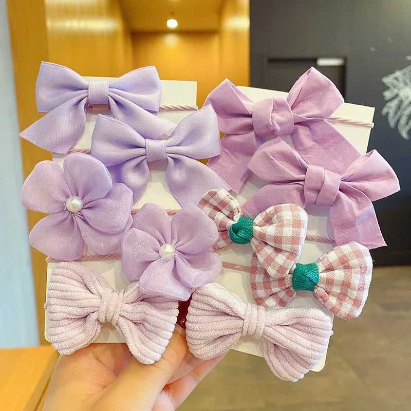 A collection of purple and pink flower bow hair ties for girls displayed on a white background.