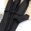 A close-up of solid black neckties folded and displayed on a woven natural fiber background.