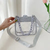 Bolso cruz de PVC transparente plateado con correa de cadena mostrado sobre una superficie blanca.
